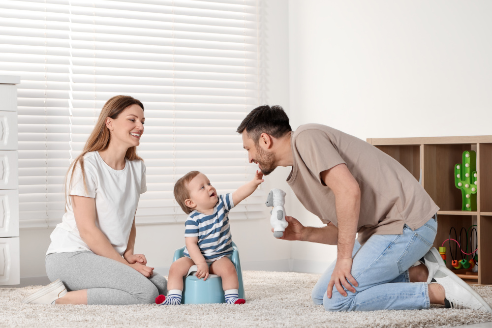 Parents training their child to sit on baby potty indoors