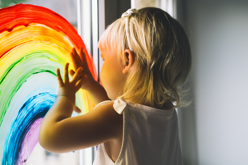 Little girl hands touch painting rainbow on window